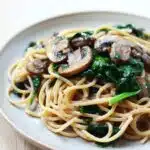 A creamy and delicious mushroom and spinach pasta served in a white bowl, garnished with fresh herbs